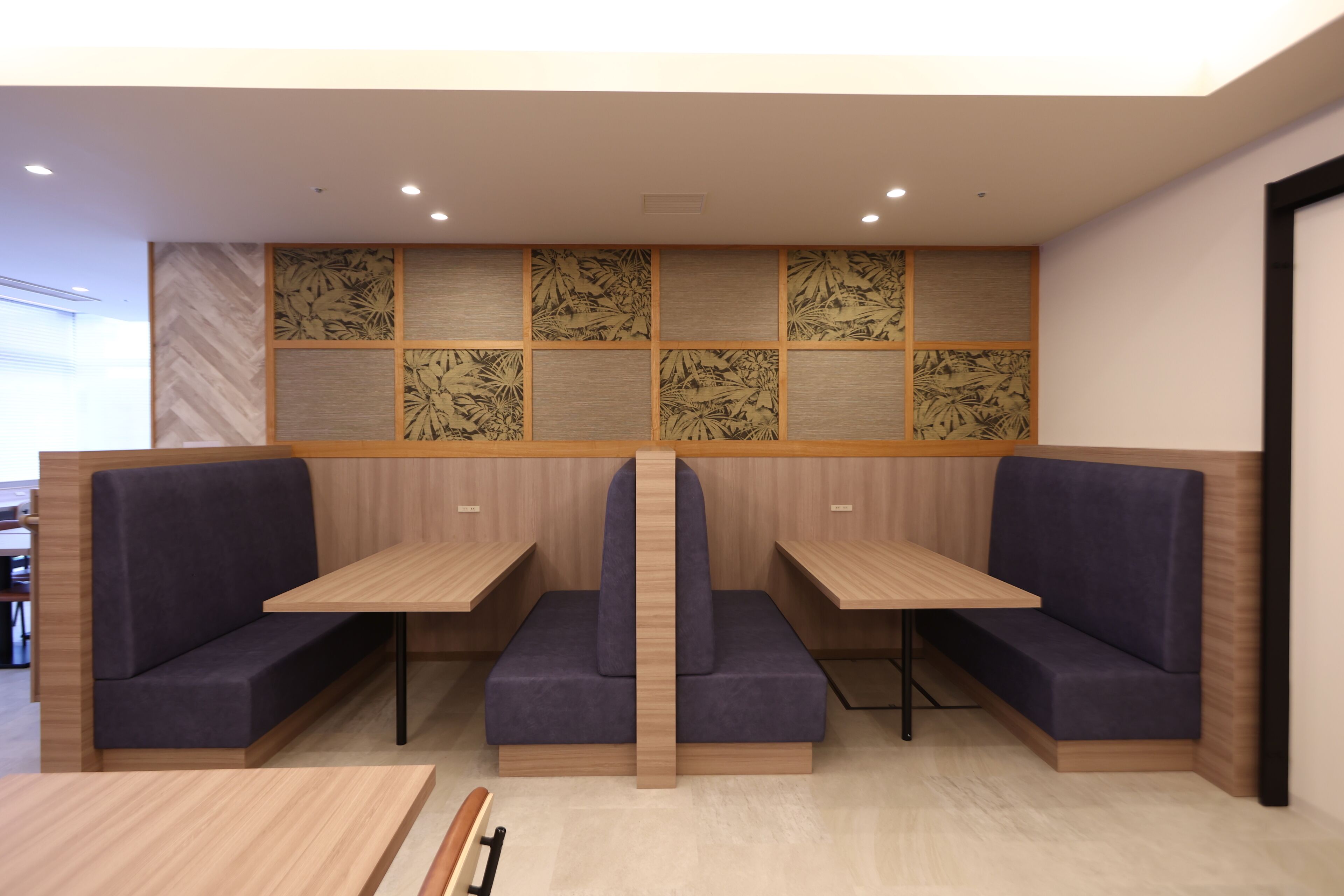 A modern seating area with wooden tables and cushioned benches, a patterned wall, and recessed ceiling lights.