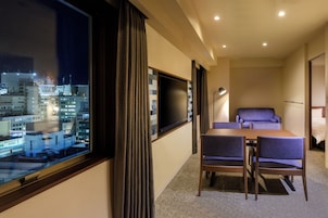 Habitación de hotel con vista a la ciudad, televisor de pantalla plana, mesa de comedor con sillas y una cama.