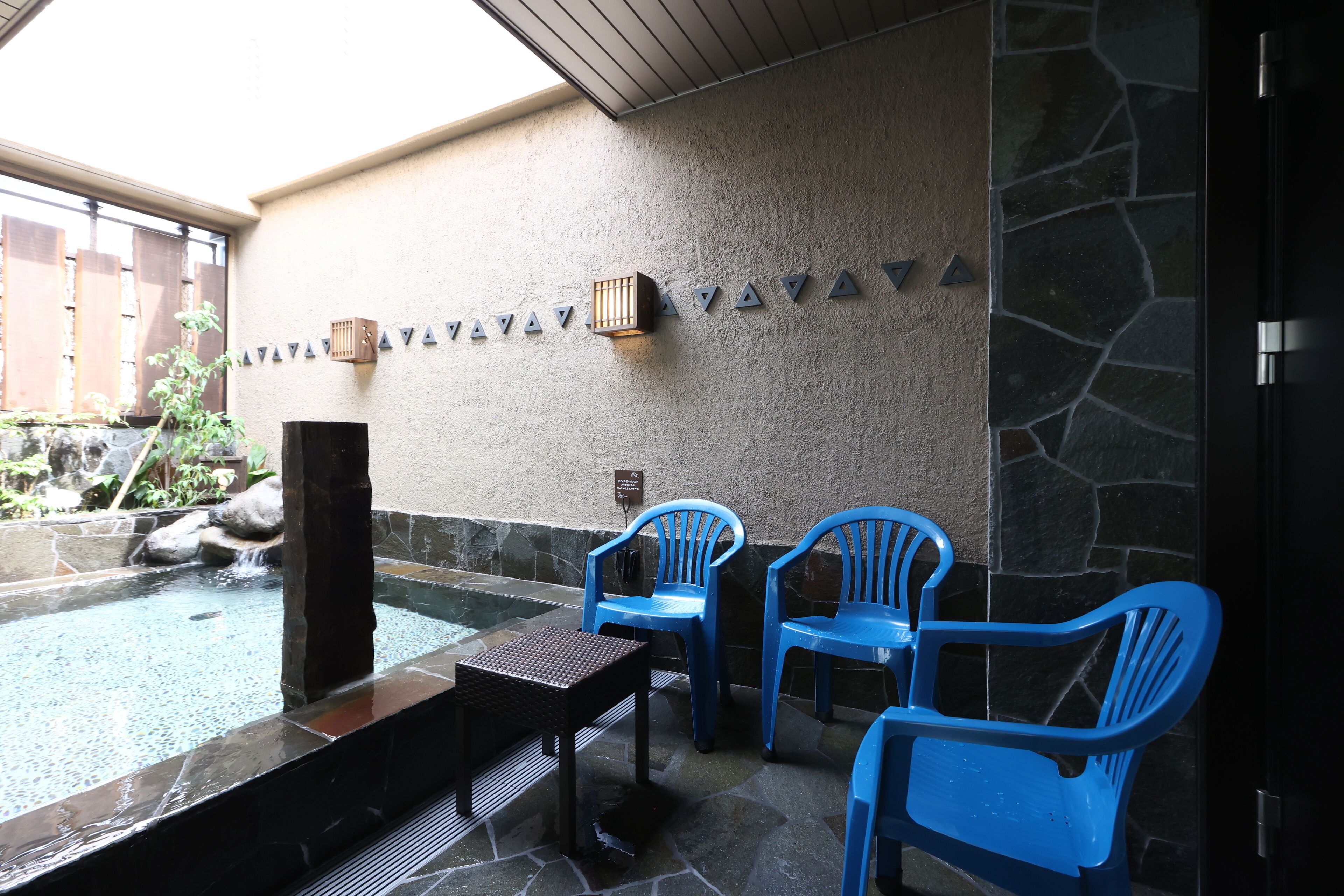 A spa area with a stone wall, a small pool, and blue plastic chairs.