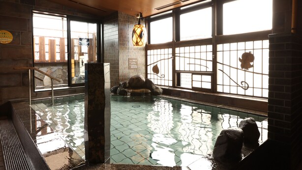 An indoor swimming pool with a tiled floor, a stone wall, and a large window with a metal gate. - Dormy Inn Okayama (Okayama)