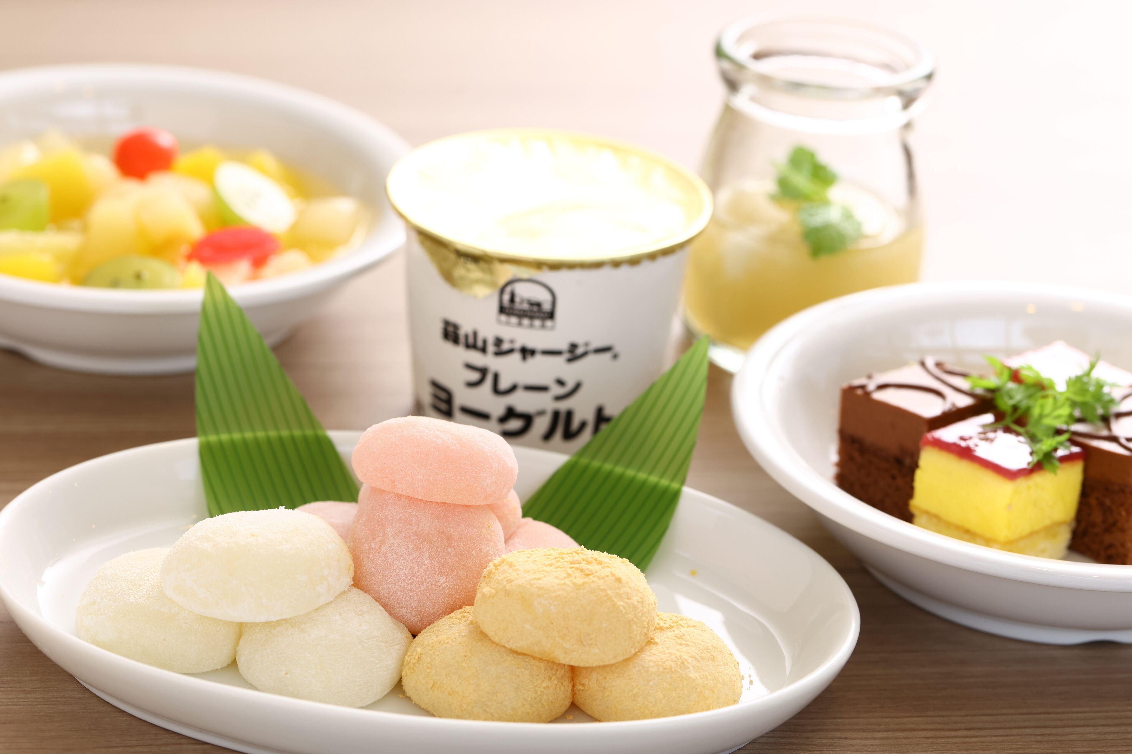Een bord kleurrijke mochi met een kleine schaal fruitsalade en een glas thee op de achtergrond.