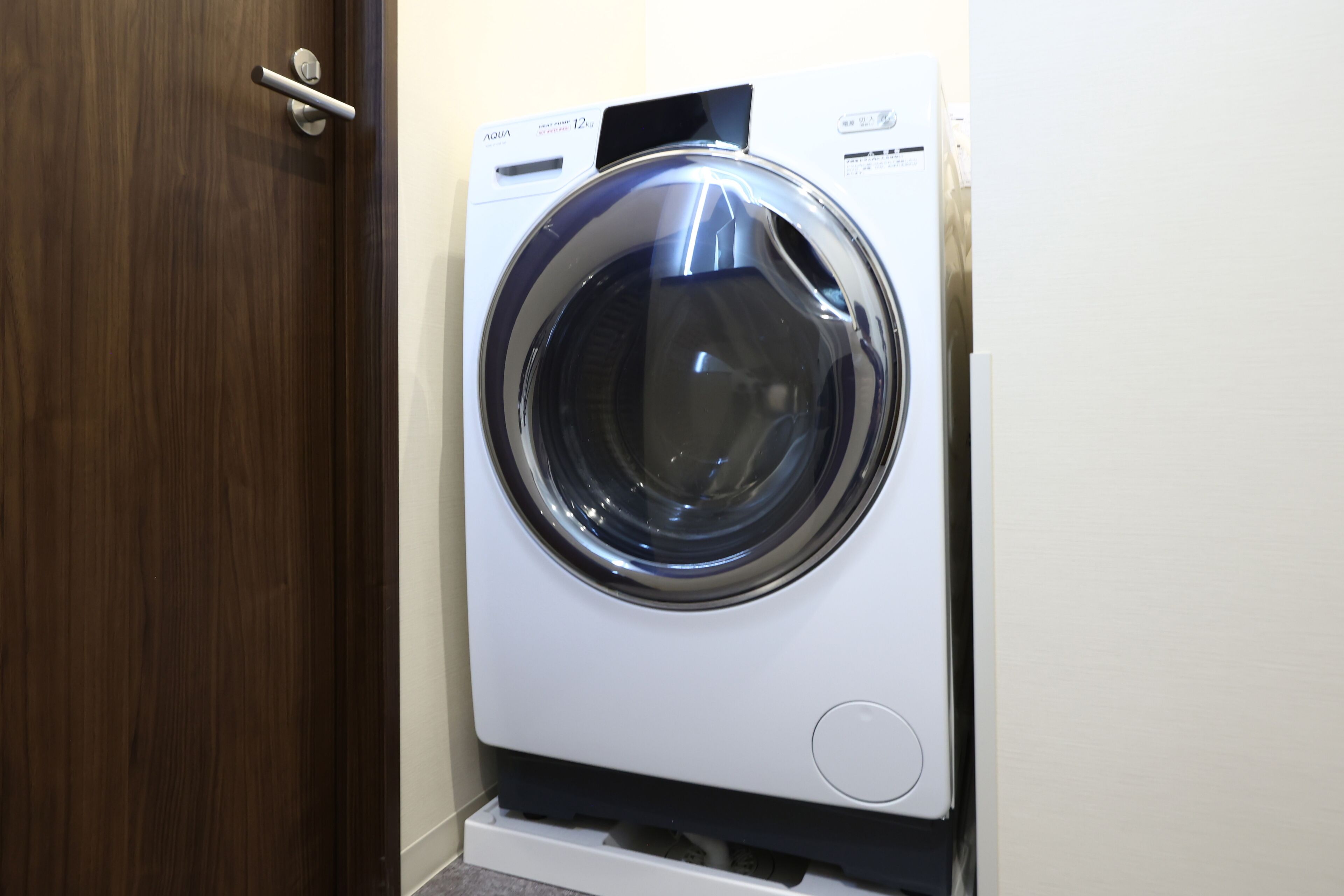 A front-loading washing machine in a laundry room with a wooden door and a white wall.