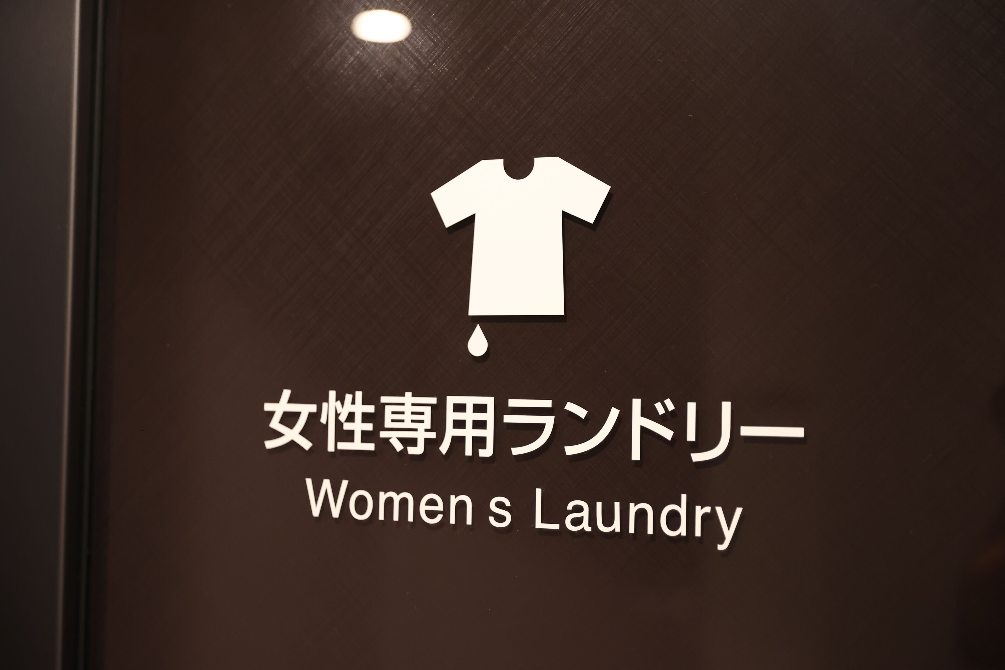A sign for "Women's Laundry" with a white t-shirt icon and Japanese text.