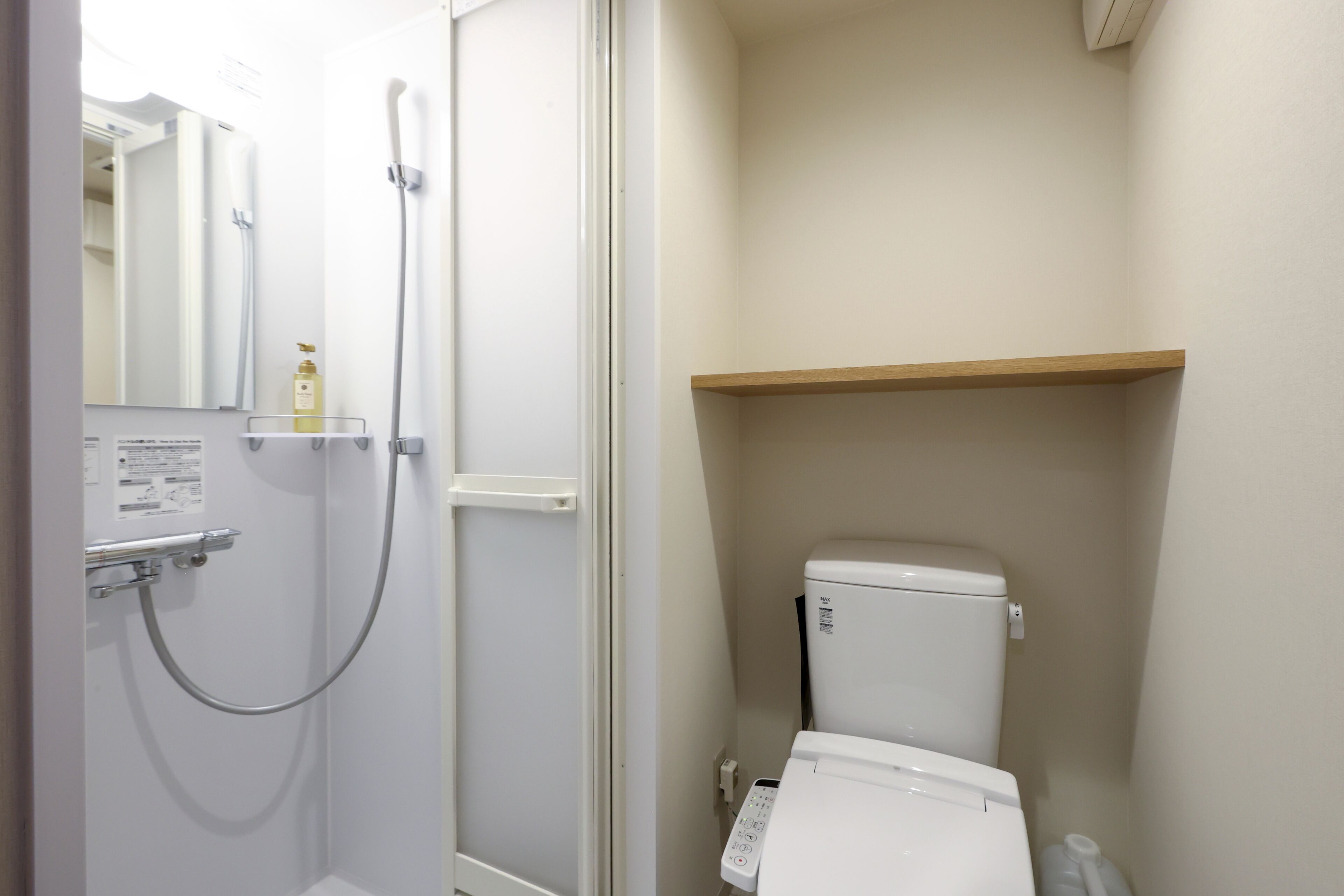 A bathroom with a shower, toilet, and a shelf above the toilet.