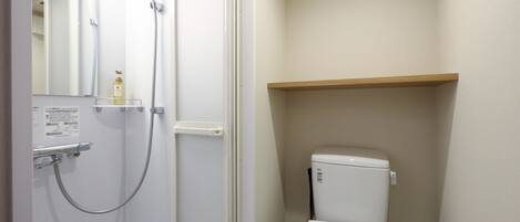 A bathroom with a shower, toilet, and a shelf above the toilet.