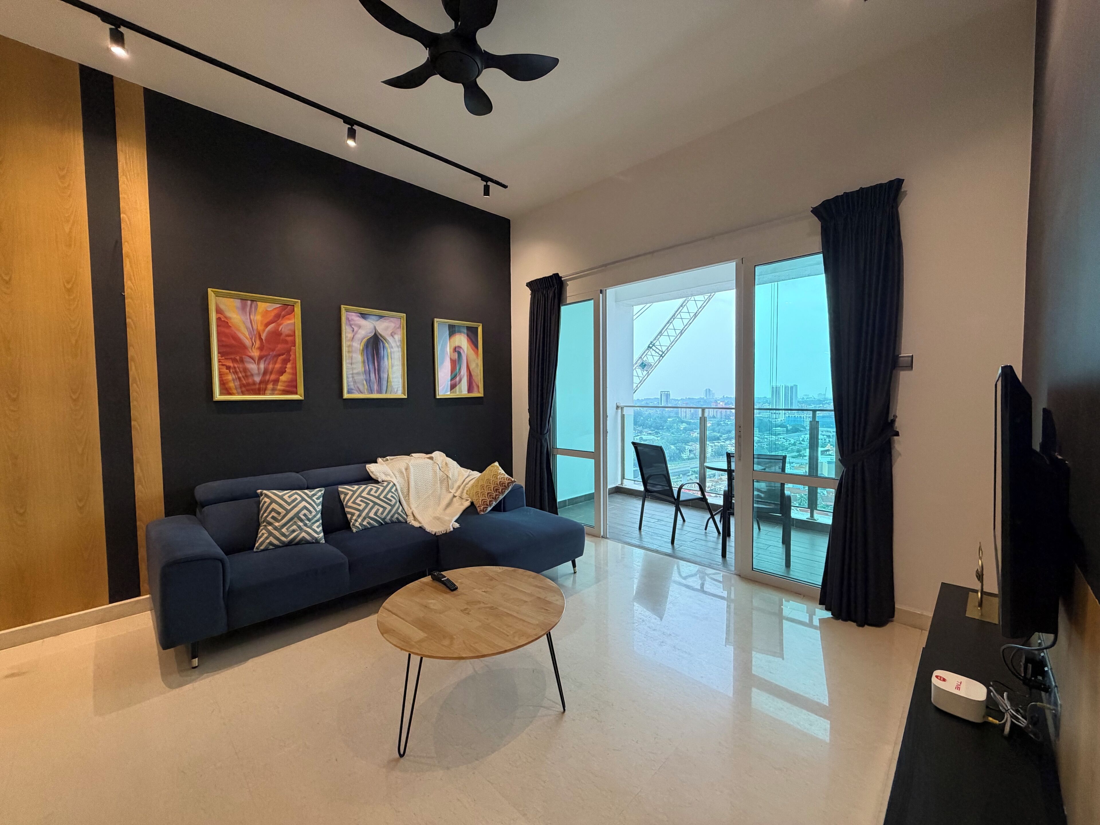 Una sala moderna con sofá, mesa de centro, obras de arte y un balcón con vistas a la ciudad.