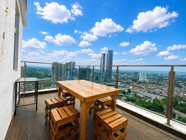 A balcony with a wooden table and benches, overlooking a cityscape with buildings and a clear sky. - Tri Tower By Antlerzone (Johor Bahru)