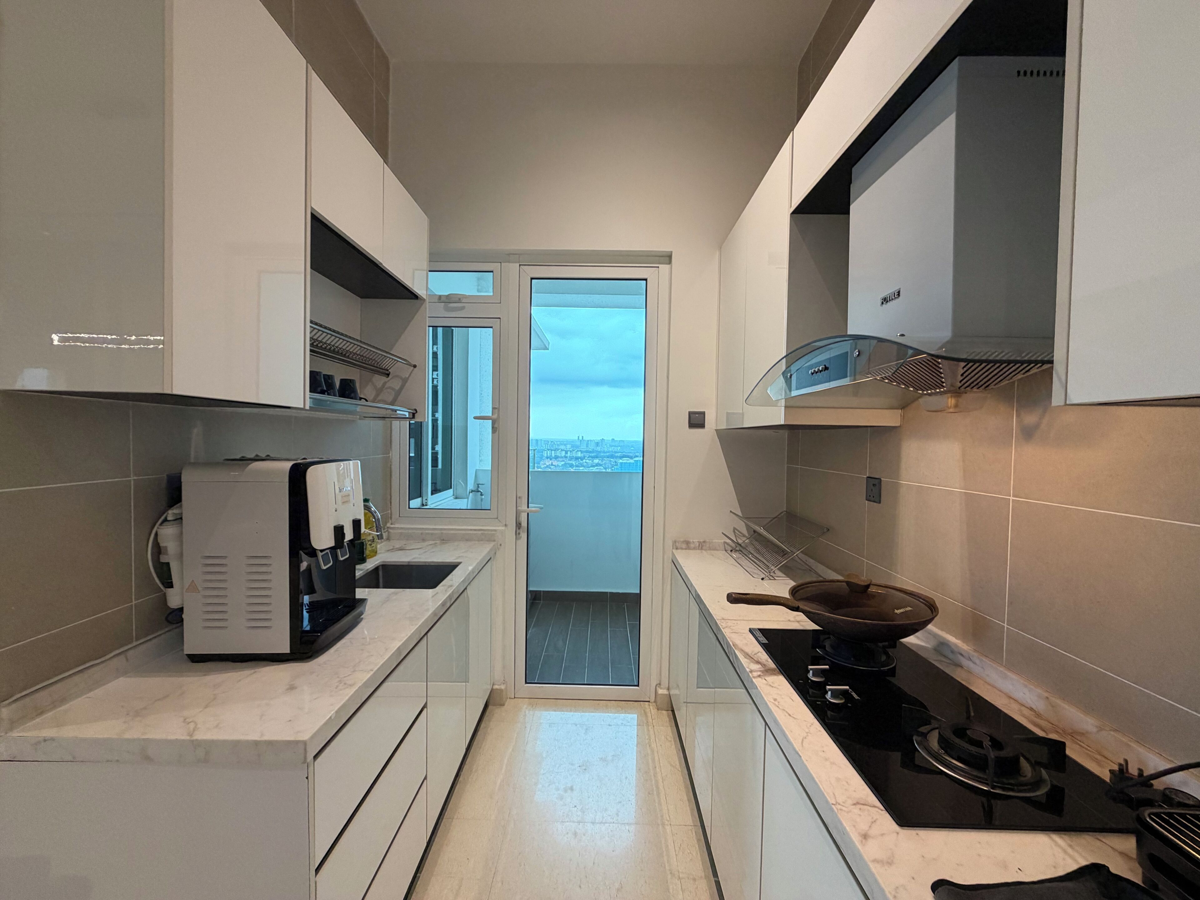A narrow kitchen with a built-in stove, a coffee machine, and a window overlooking a cityscape.