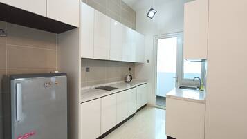 A modern kitchen with white cabinets, a stainless steel refrigerator, a kettle, and a window providing natural light.