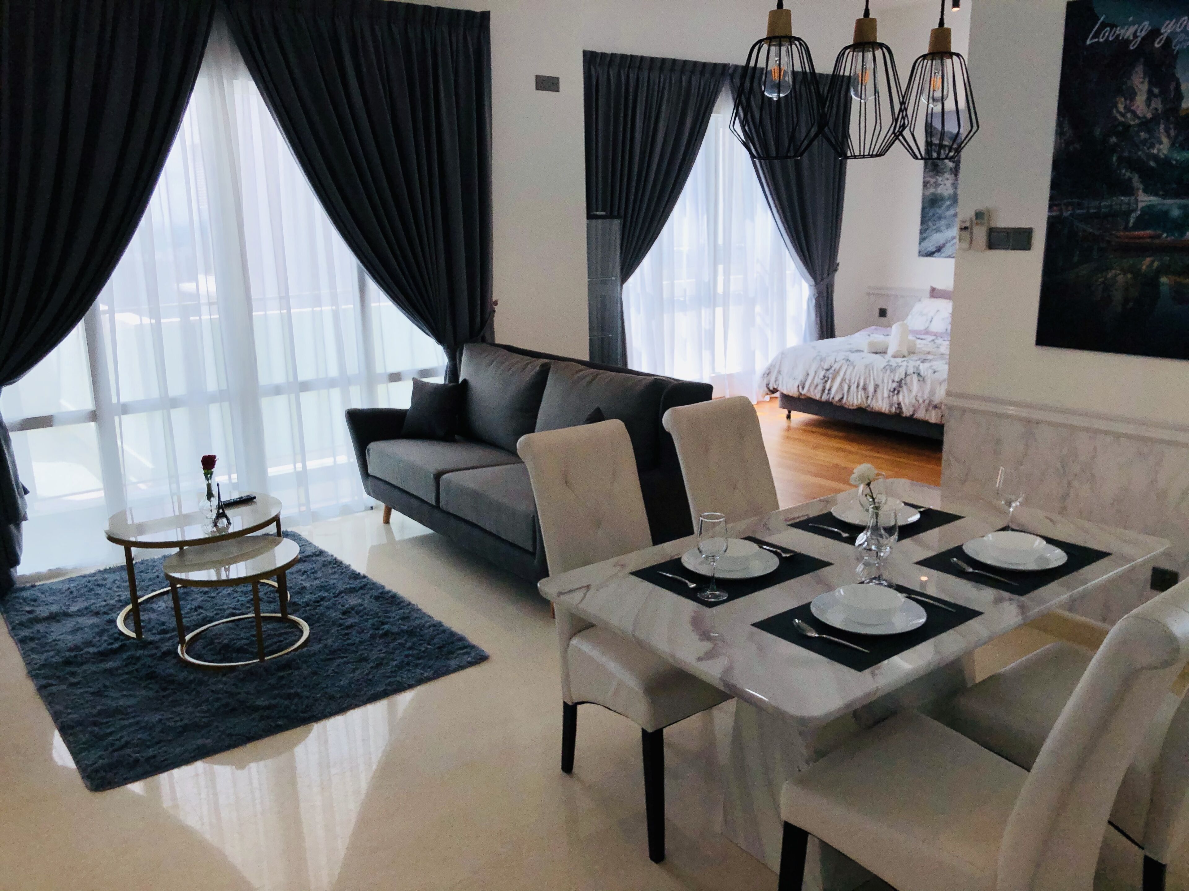 A modern living room with a dining area, a sofa, a coffee table, and a bed with a view.