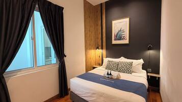 A hotel room with a bed, a window with curtains, a wall-mounted lamp, and a framed picture.