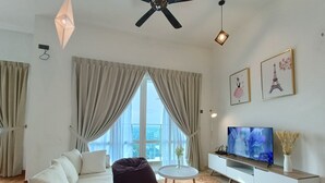 A modern living room with a white sofa, a dark bean bag, a round coffee table, and a flat-screen TV on a white TV stand. - Tri Tower By Antlerzone (Johor Bahru)