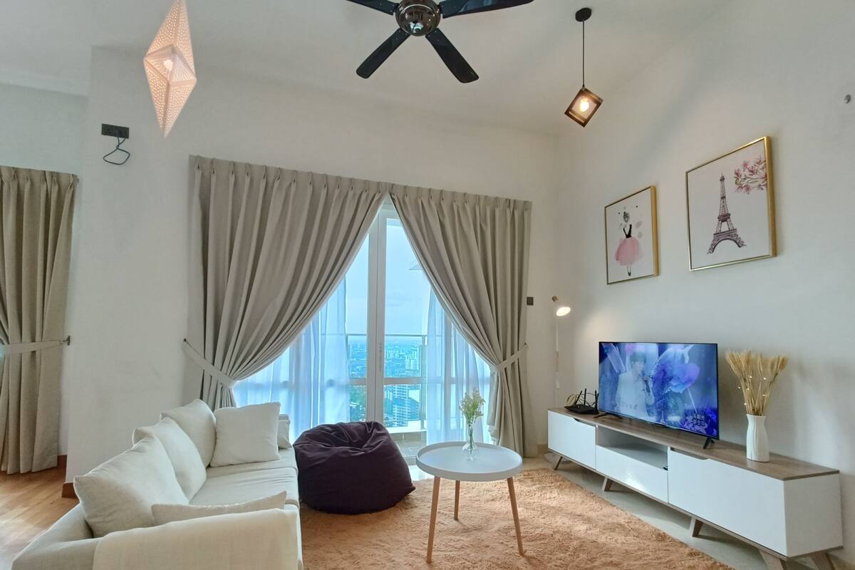 A modern living room with a white sofa, a dark bean bag, a round coffee table, and a flat-screen TV on a white TV stand.