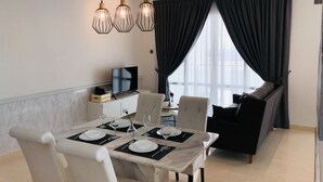 A dining area with a table set for four, a television on a cabinet, and a dark-colored sofa in the background. - Tri Tower By Antlerzone (Johor Bahru)