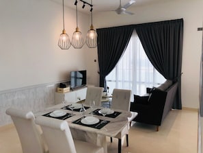 A dining area with a table set for four, a television on a cabinet, and a dark-colored sofa in the background. - Tri Tower By Antlerzone (Johor Bahru)