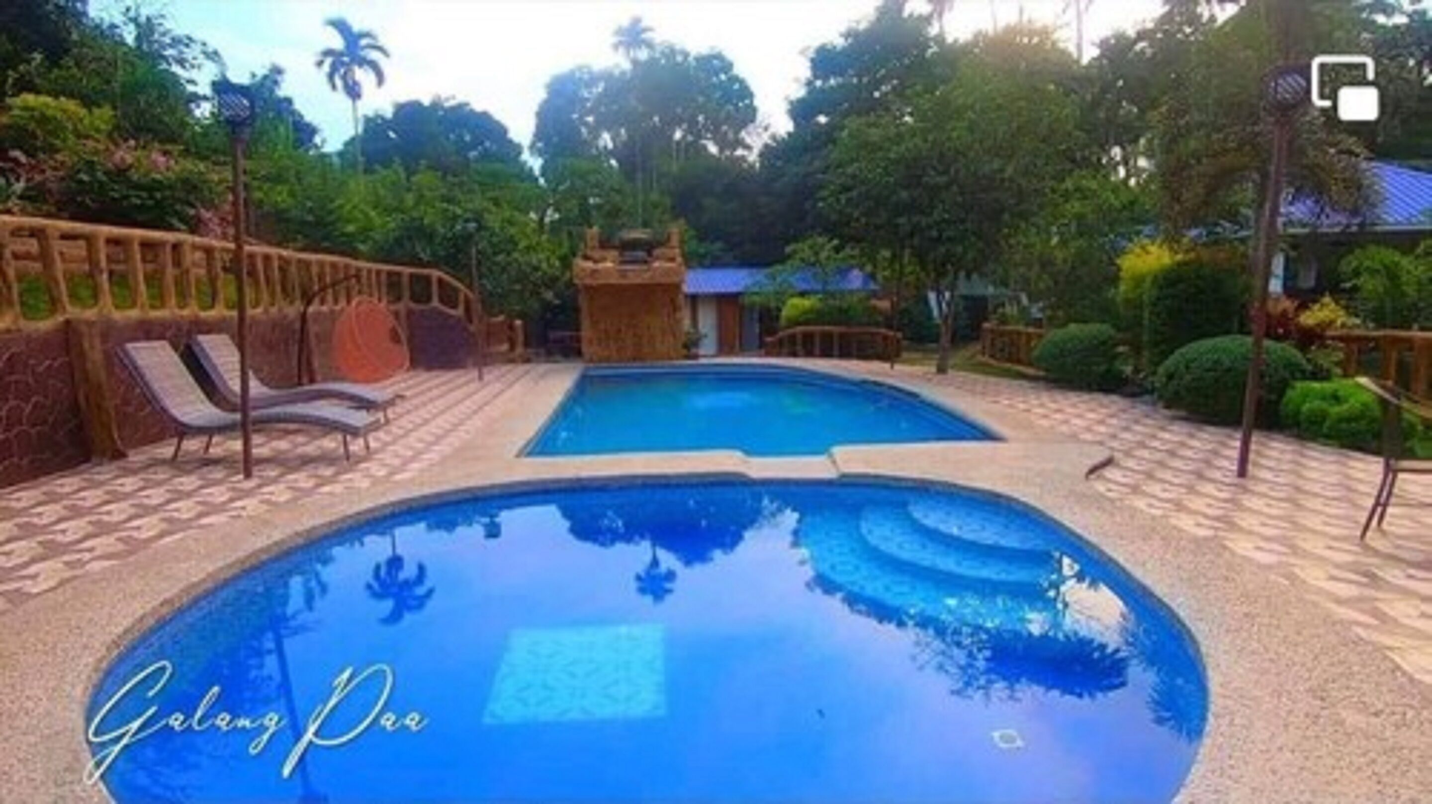 A swimming pool with lounge chairs and a wooden structure in the background.