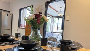 A dining area with a wooden table set for two, including plates, bowls, cutlery, and a vase with flowers. - Modern than 3 bedroom house  with office space in the center of Kallangur (Kallangur)