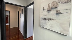 A hallway with wooden flooring and a framed landscape painting of a beach scene. - Modern than 3 bedroom house  with office space in the center of Kallangur (Kallangur)