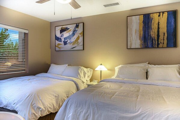 A hotel room with two beds, a ceiling fan, and two abstract paintings on the walls.