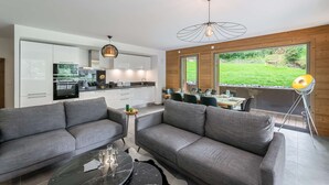 A modern living room with a grey sofa, a black coffee table, and a dining area with a wooden table and chairs. - Apartment Quintessence - B101 (CHATEL)