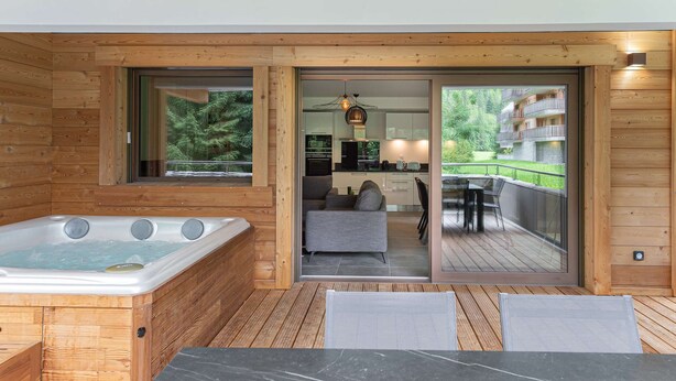 A wooden cabin with a hot tub, a dining area, and a view of a balcony with outdoor furniture. - Apartment Quintessence - B101 (CHATEL)