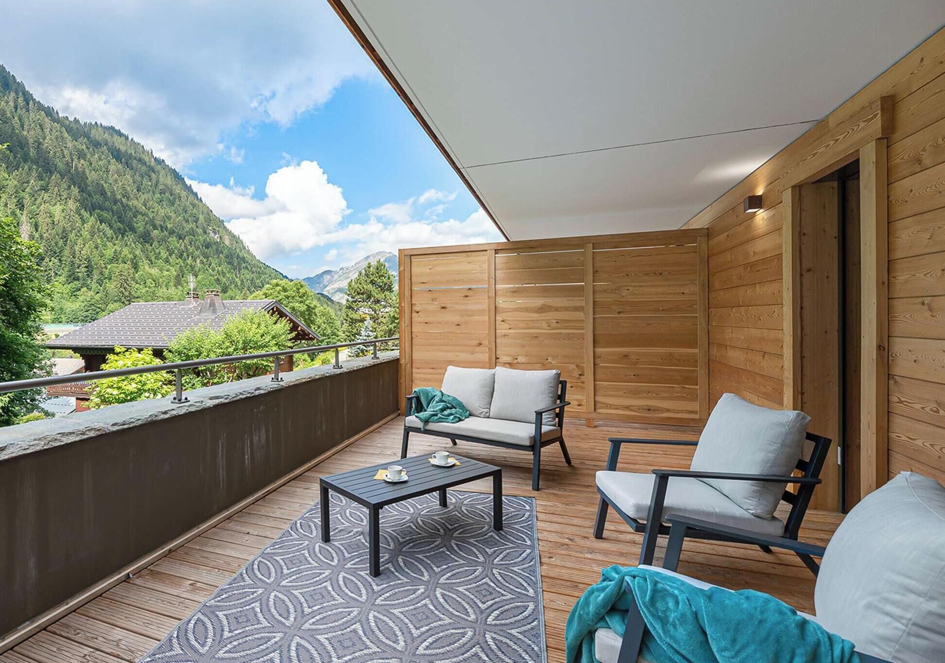 Een houten balkon met een bank, stoelen en een tafel.