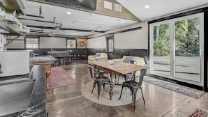 Uma sala de estar ampla com uma grande mesa de madeira, assentos confortáveis e vista através de uma porta de vidro deslizante.