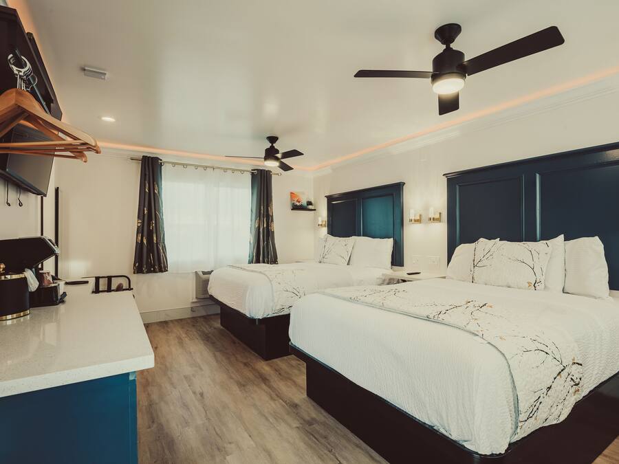 Une chambre d’hôtel avec deux lits, un bureau, un ventilateur de plafond et une télévision.