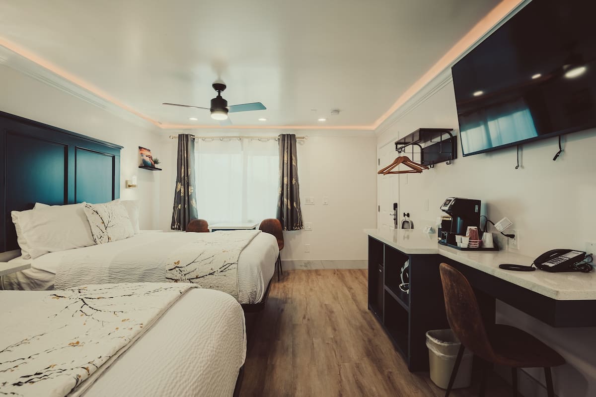 A modern hotel room with two beds, a desk, a TV, and a ceiling fan.