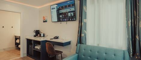 A modern room with a blue sofa, a desk with a computer, and a TV mounted on the wall.