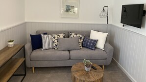 A living room with a grey sofa, a round wooden coffee table, a small plant, and a framed picture on the wall. - Starfish Shack Apartment @ Sunnybeach (Paignton)