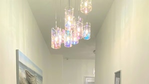 Un couloir avec un tapis noir, des murs blancs, un tableau représentant un bateau, un distributeur de gel hydroalcoolique et une porte au fond.