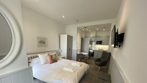 Une chambre avec un grand lit, un bureau et, au fond, un coin cuisine.