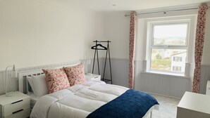 Une chambre à coucher comprenant un lit, une table de chevet, un portant à vêtements et une fenêtre avec des rideaux.