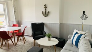 Un salon moderne avec un canapé blanc, des fauteuils rouges, un fauteuil noir, une table ronde blanche et une plante en pot.