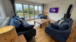 A living room with two blue sofas, a wooden coffee table, and a television displaying 'Absolute Radio'. - Holly Cottage @ Arrowan Common Farm (Coverack)