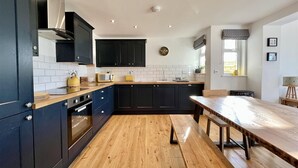 A modern kitchen with dark cabinets, a wooden countertop, and a wooden dining table. - Holly Cottage @ Arrowan Common Farm (Coverack)