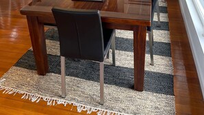 Ein Essbereich mit einem Holztisch, schwarzen Stühlen, einem Teppich und Blick auf einen Holzzaun.