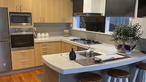 Eine moderne Küche mit Holzausstattung, Einbauofen, Mikrowelle, Gaskochfeld und einer großen Kochinsel mit Hockern.
