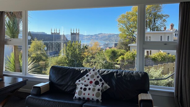 Ein Wohnzimmer mit schwarzem Ledersofa, Blick auf ein Dom und eine Stadtansicht.
