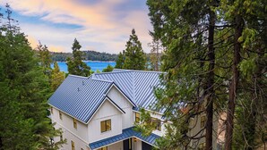 A two-story house with a blue metal roof, surrounded by trees and a view of a lake.