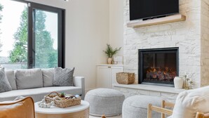 A modern living room with a fireplace, a sofa, ottomans, and a television mounted on the wall.