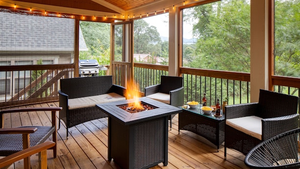 A covered outdoor deck with a fire pit, wicker furniture, and string lights. - Covered Deck + Firepit | Black Mountain Retreat | Sweetgum by AvantStay (Black Mountain)