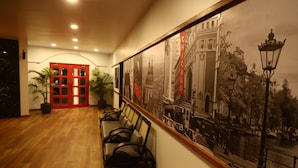 A hallway with wooden flooring, a red door, and a wall with a cityscape mural. - Annandam Inn-Hotel Anand (Seoni)