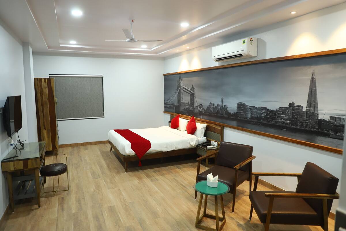 Ein Hotelzimmer mit Bett, zwei Stühlen, einem kleinen Tisch, einem Fernseher und einem Stadtbild an der Wand.