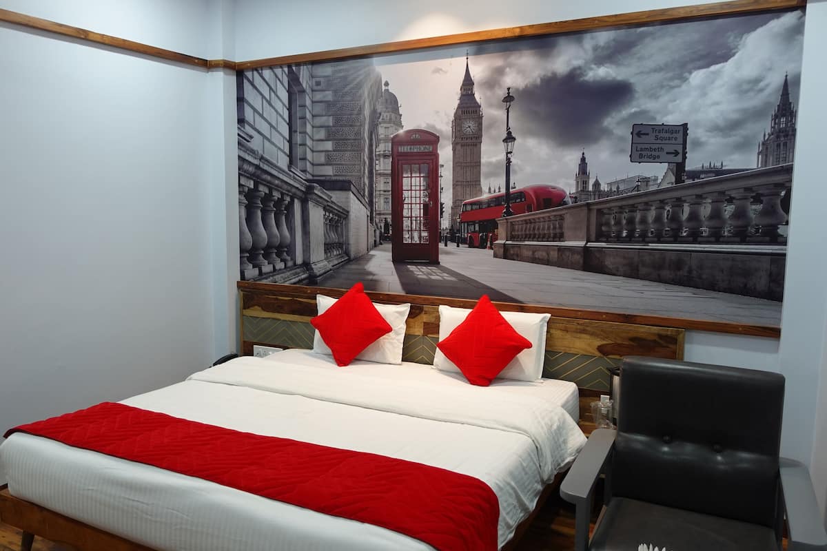 Ein Hotelzimmer mit einem großen Stadtbild-Wandgemälde, einem Bett mit roter und weißer Bettwäsche sowie einem schwarzen Stuhl.