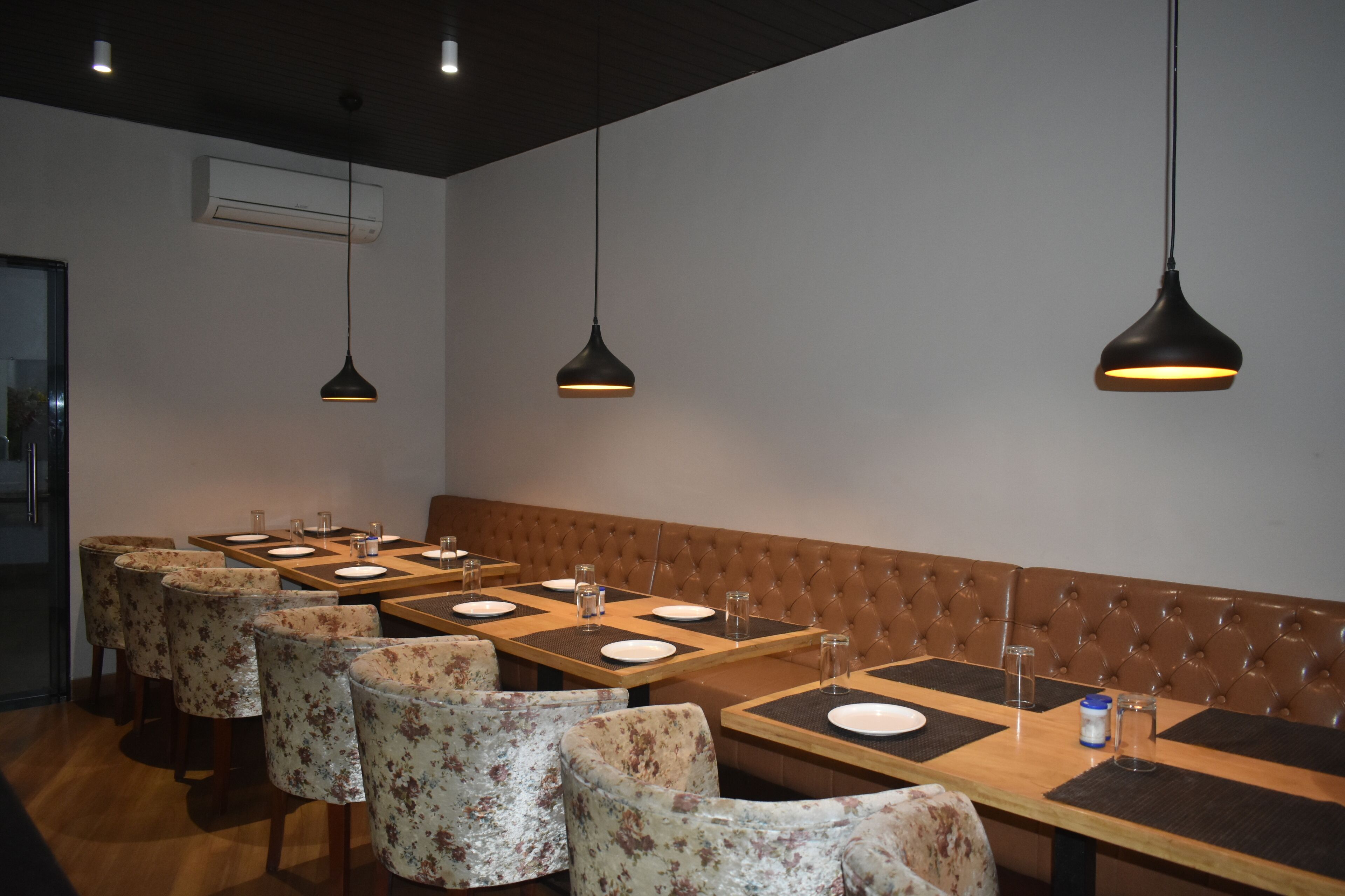 Un restaurante con una larga mesa de madera y asientos tapizados, iluminación colgante y un equipo de aire acondicionado instalado en la pared.