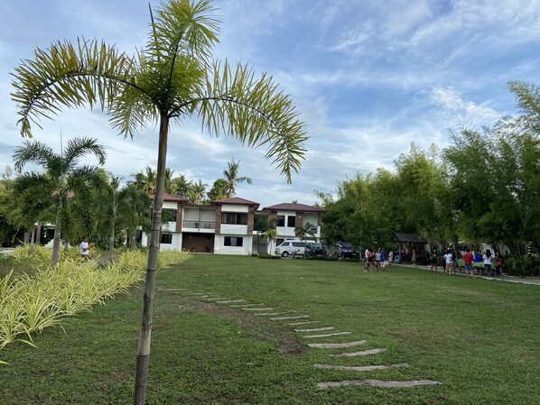 A residential area with a grassy lawn, palm trees, and a two-story house with a balcony.