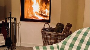 A cozy living room with a fireplace, a wicker basket with logs, and a checkered sofa. - Comfortable (122m2) 1.2km from the beach (Jard-sur-Mer)