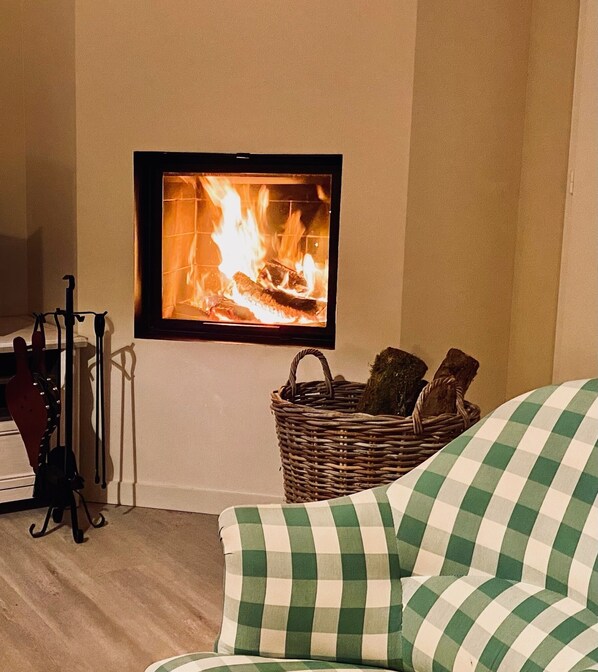Una sala de estar acogedora con chimenea, una cesta de mimbre con leños y un sofá a cuadros.